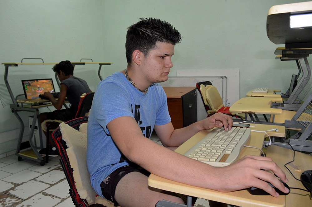 Dos jóvenes usan computadoras en salón de un joven club.