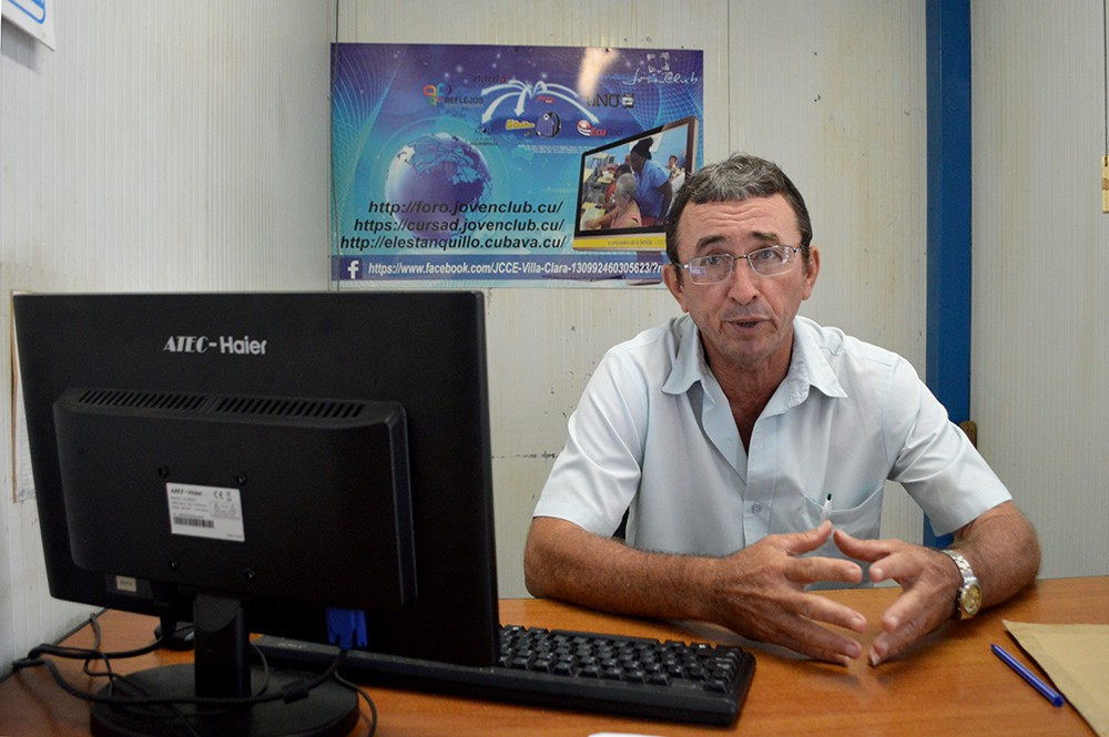 Instructor de joven club sentado frente a una computadora en un buró.