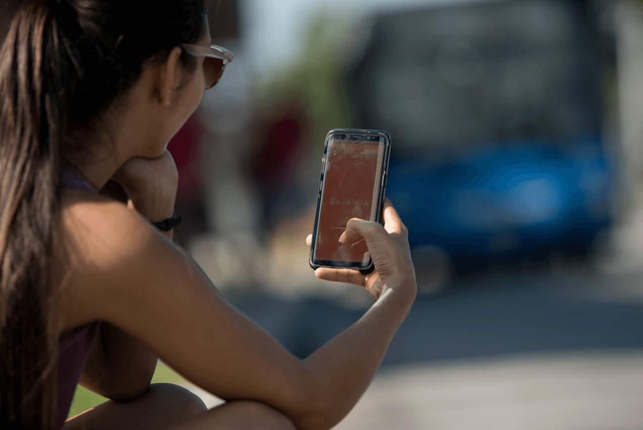 Muchacha sostiene teléfono movil en la calle. En la pantalla se observa la app Bajanda, una versión cubana de Uber