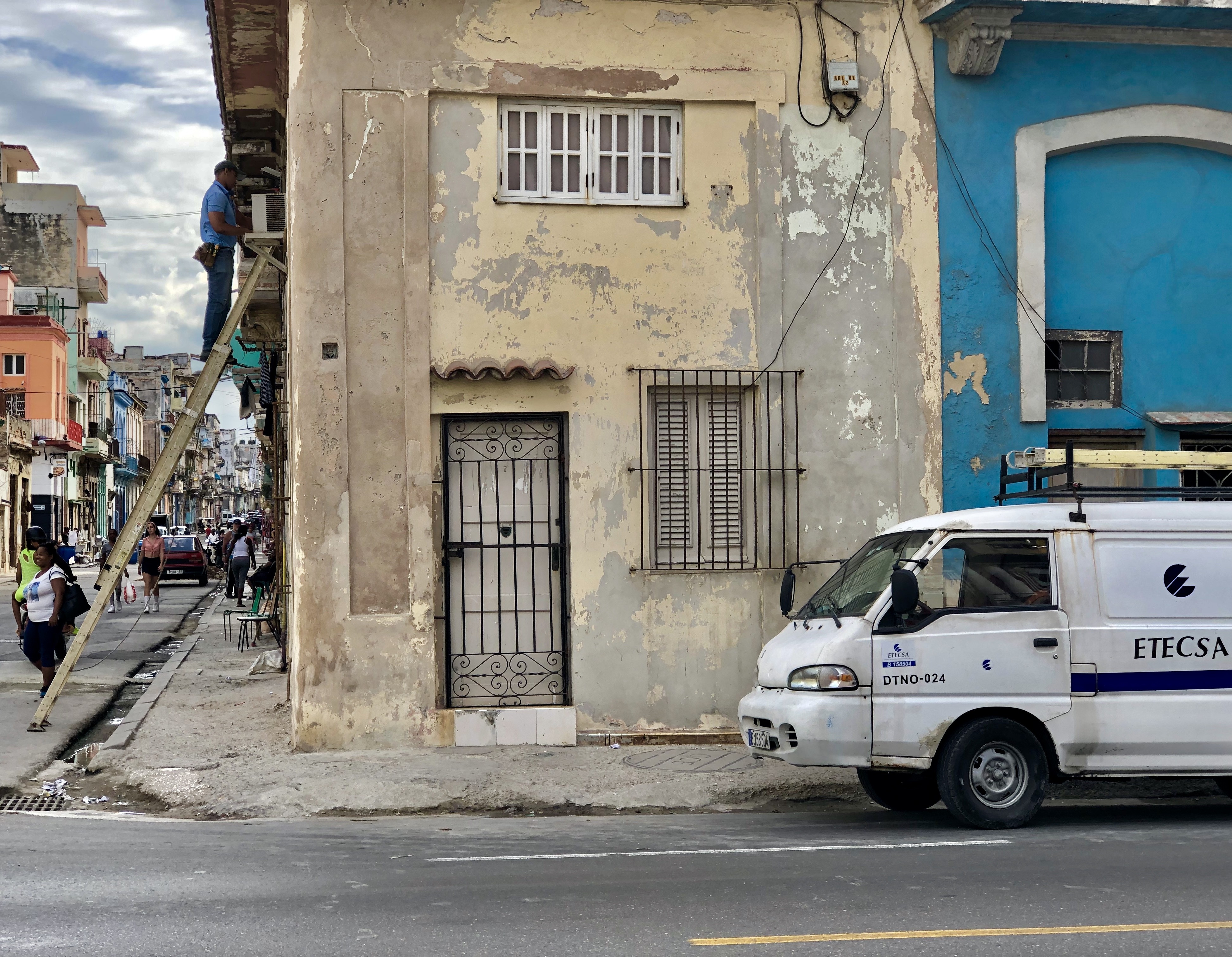 Trabajador de ETECSA repara, montado en una escalera, el cableado telefónico de un casa en una calle de La Habana