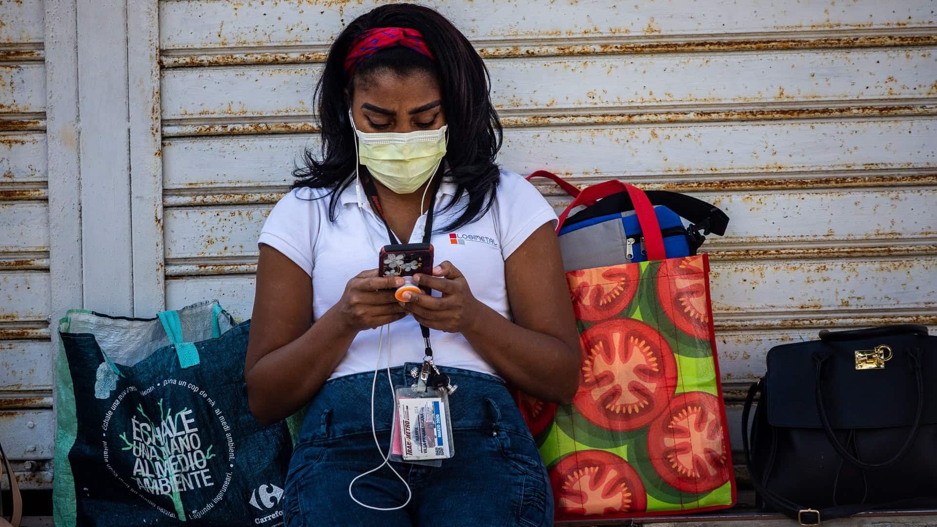 Cubana revisa su teléfono móvil con una mascarilla (nasobuco) en la boca para evitar la propagación del coronavirus