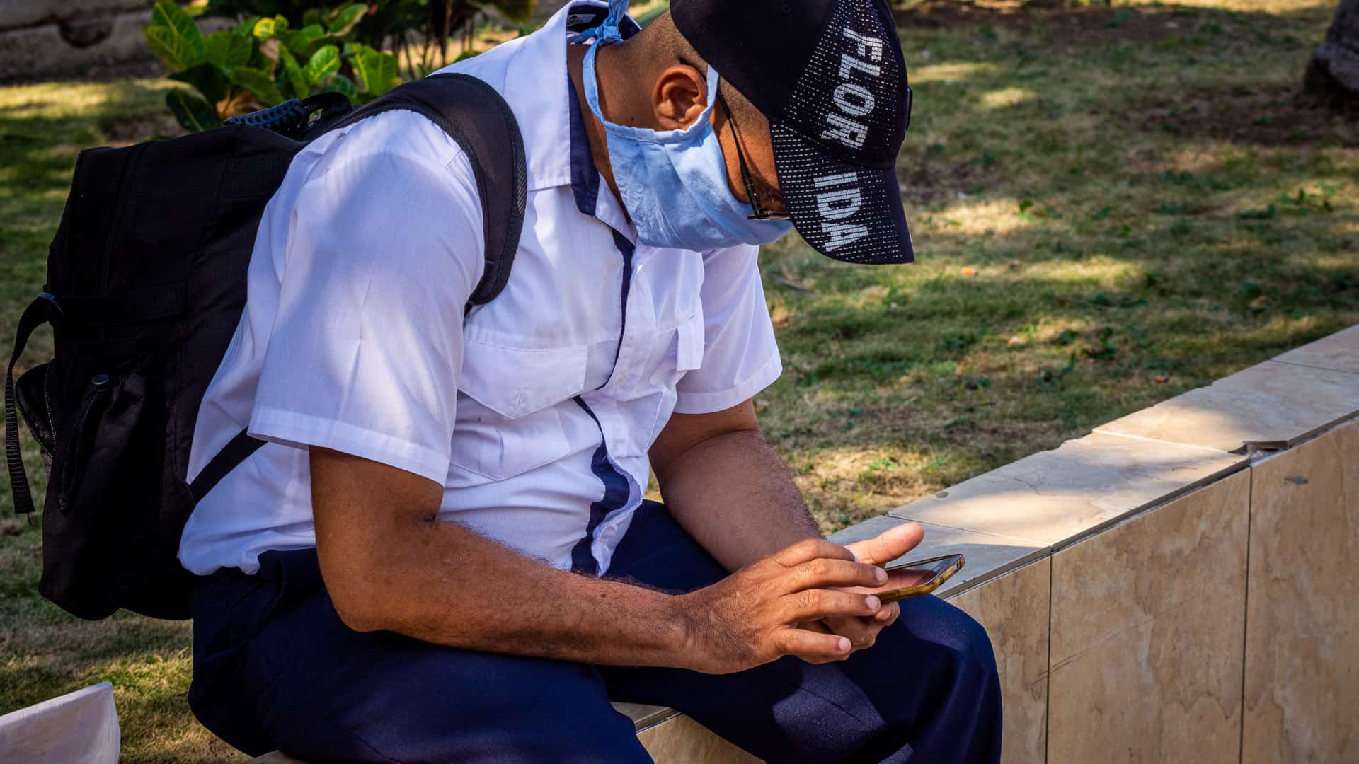 Hombre sentado en un parque con su teléfono y un nasobuco