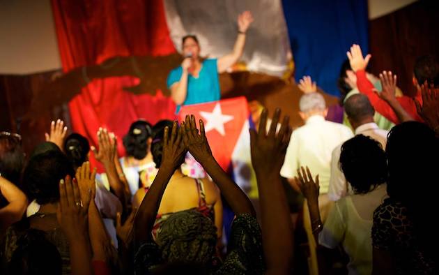 Manos de personas en un culto y bandera cubana